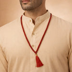 Man wearing a red beaded necklace with a tassel on a beige background