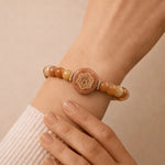 Close-up of a wrist wearing a beaded bracelet with a central circular design on a beige background
