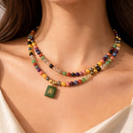 Colorful beaded necklace with a green pendant on a person wearing a white top.