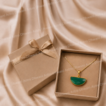 Gold necklace with a green pendant in an open box on a beige fabric background