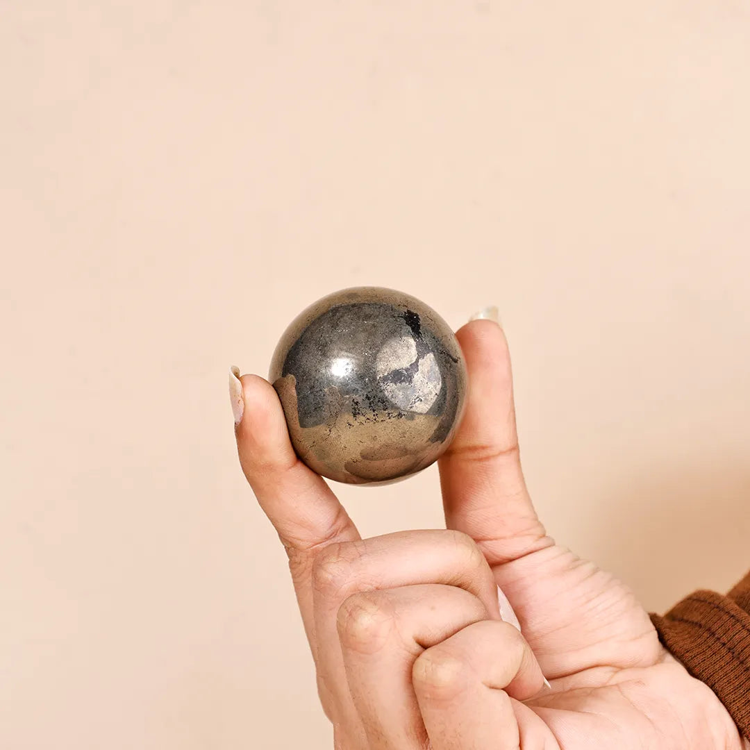 Hand holding a small, round, metallic object against a beige background