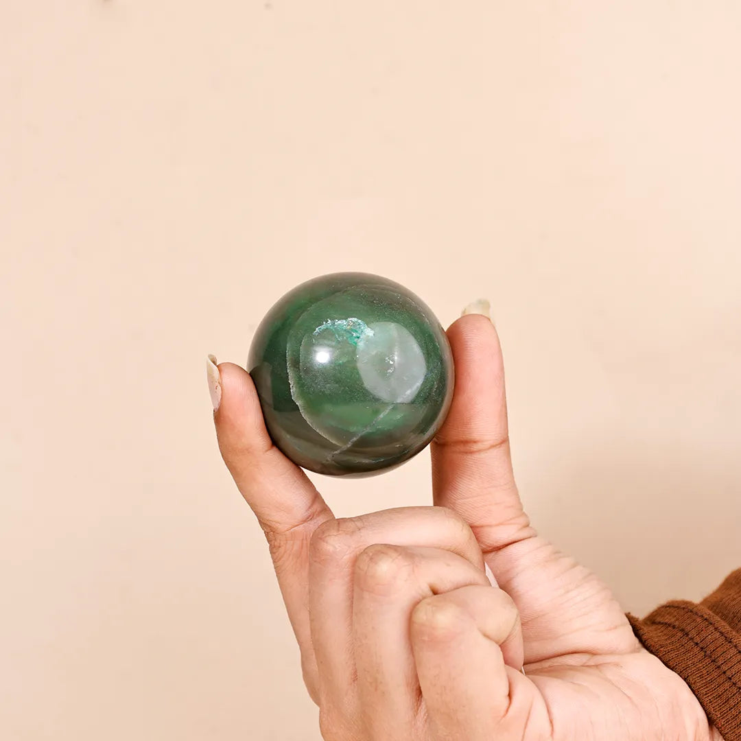 Hand holding a green crystal ball against a beige background