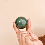 Hand holding a green crystal ball against a beige background