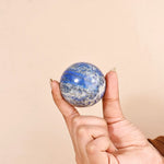 Hand holding a blue and white marbled sphere against a beige background