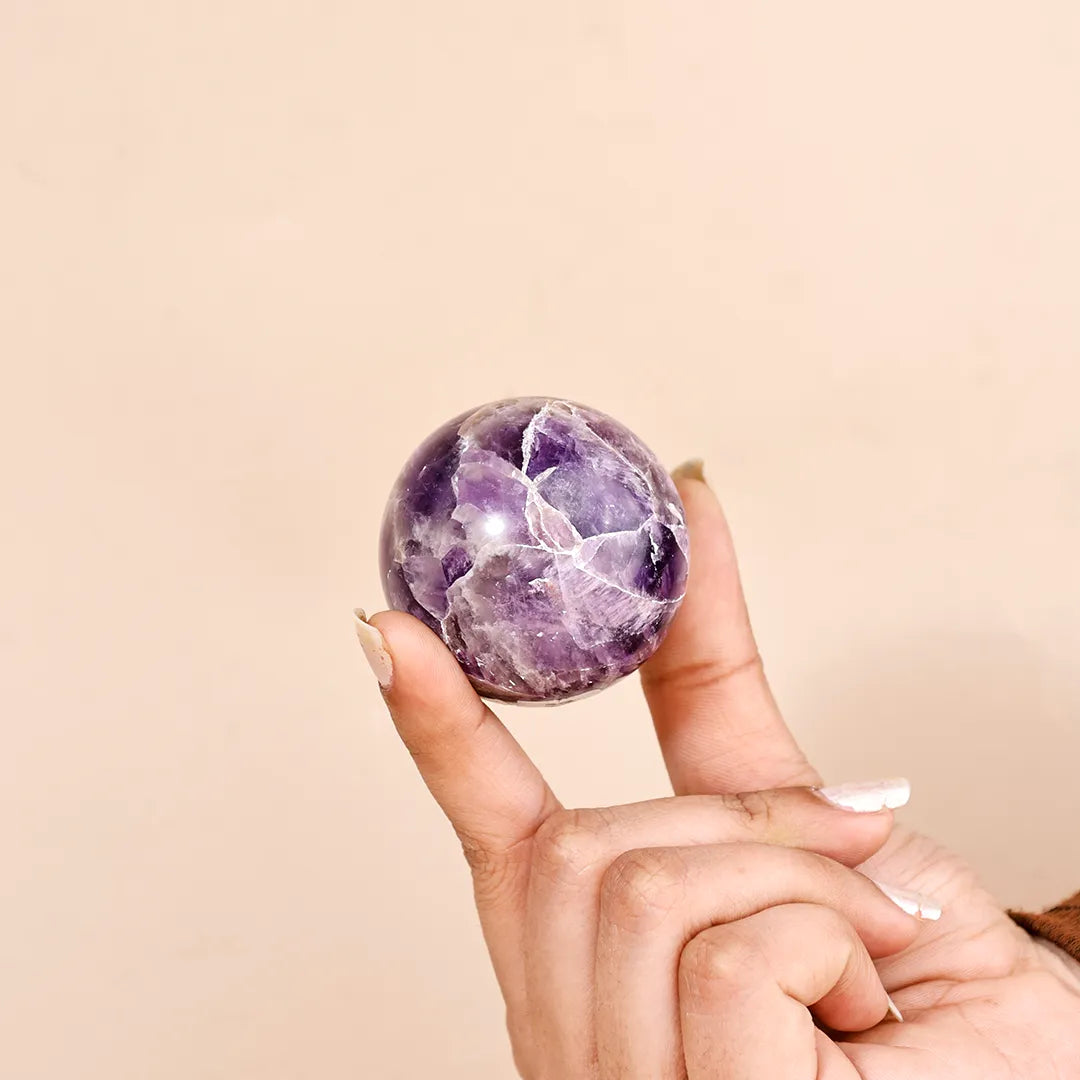 Hand holding a purple amethyst crystal ball against a beige background