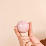Hand holding a pink crystal ball against a beige background