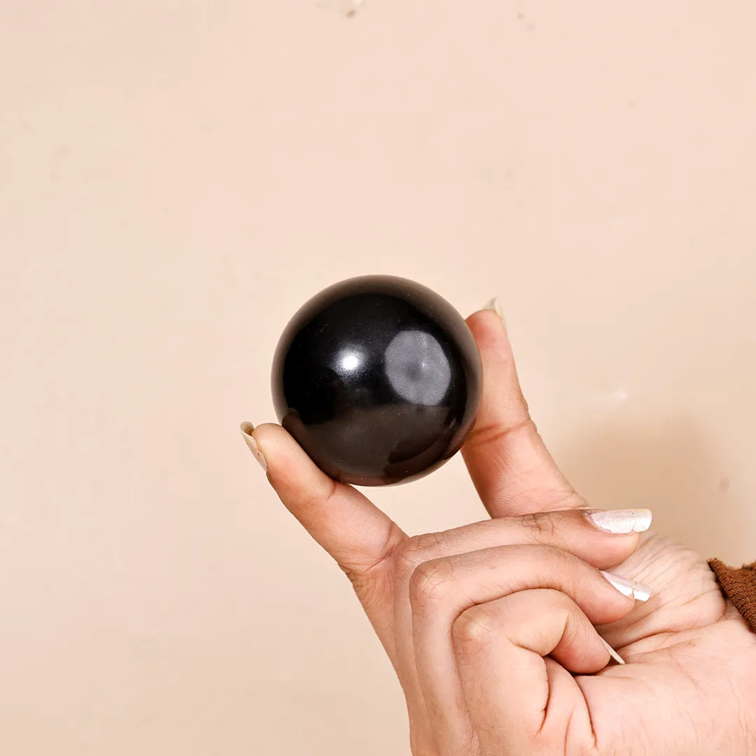 Hand holding a black sphere against a beige backgroundNatural Black Agate Crystal Ball – Abhimantrit & Certified