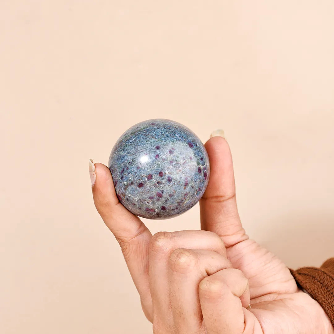 Hand holding a speckled blue and purple ball against a beige background