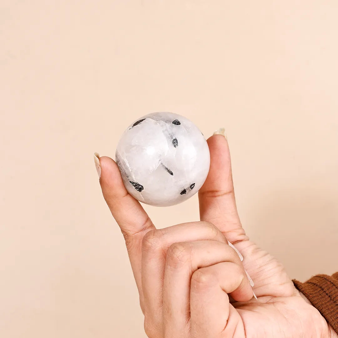 Hand holding a marbleized sphere against a beige backgroundNatural Black Rutilated Quartz Crystal Ball – Abhimantrit & Certified