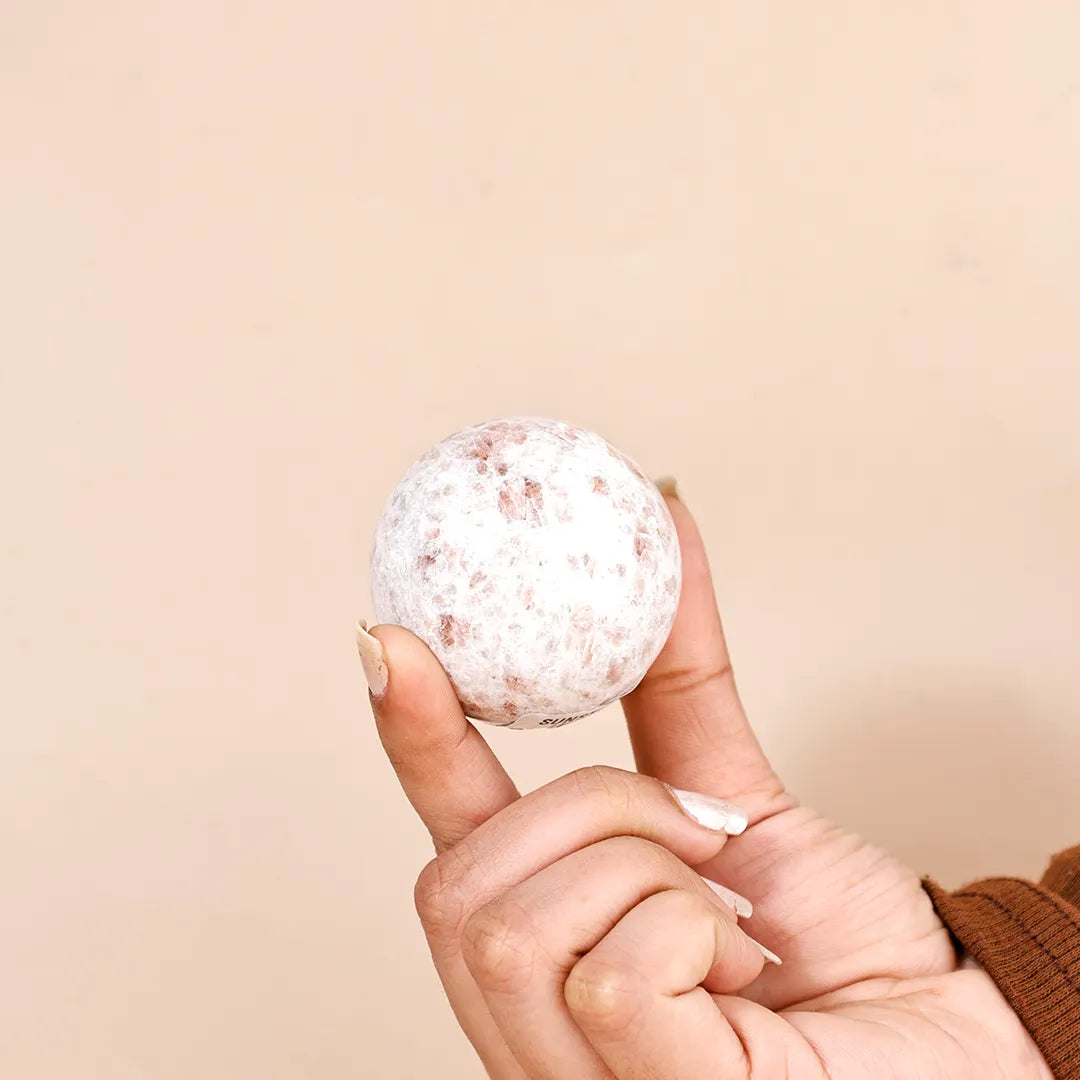 Hand holding a bath bomb against a beige backgroundNatural Sunstone Crystal Ball – Abhimantrit & Certified