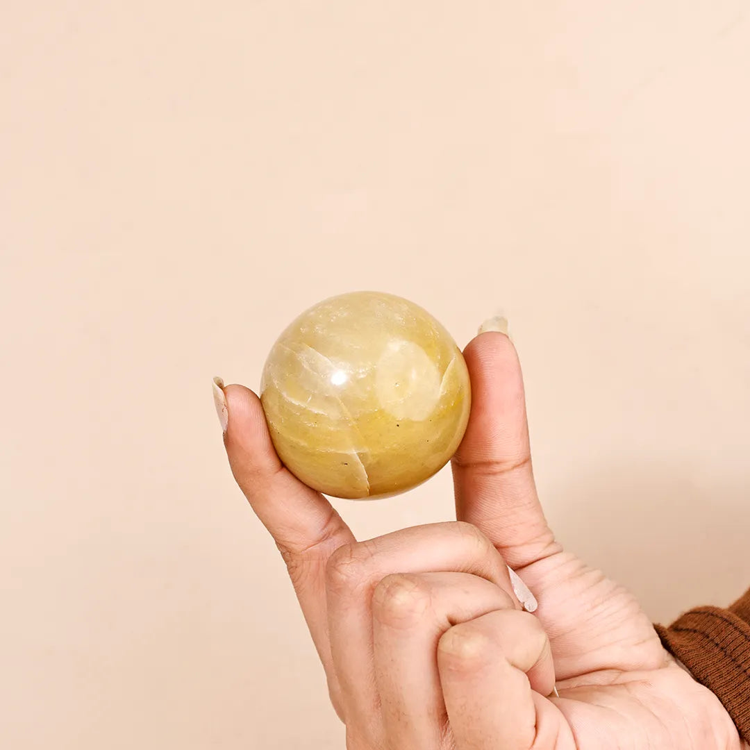 Hand holding a yellow crystal ball against a beige backgroundNatural Yellow Aventurine Crystal Ball – Abhimantrit & Certified