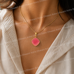 Necklace with a pink pendant worn by a person in a light-colored outfit.