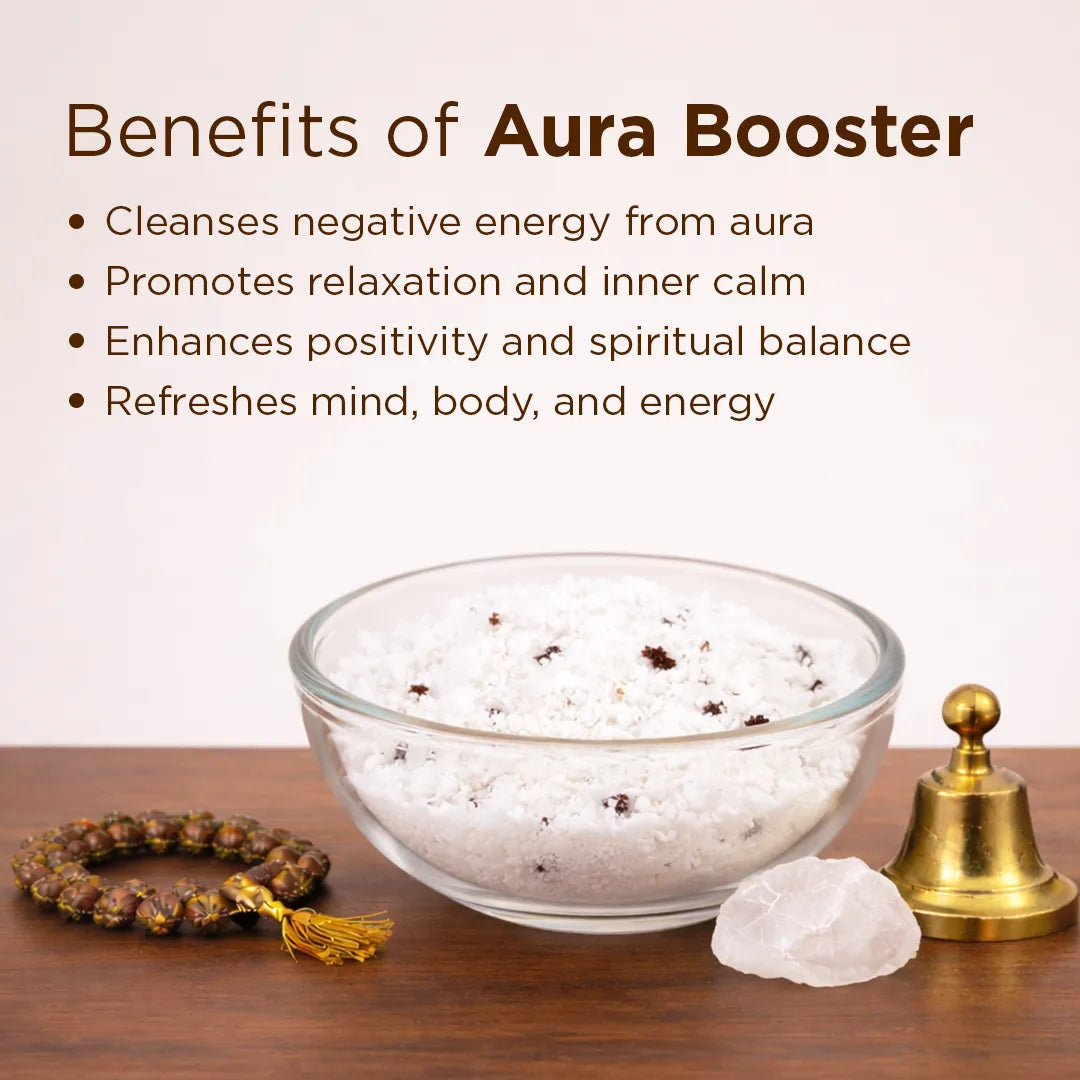 Bowl of salt, crystal, bell, and bracelet with 'Benefits of Aura Booster' text on a wooden surface.