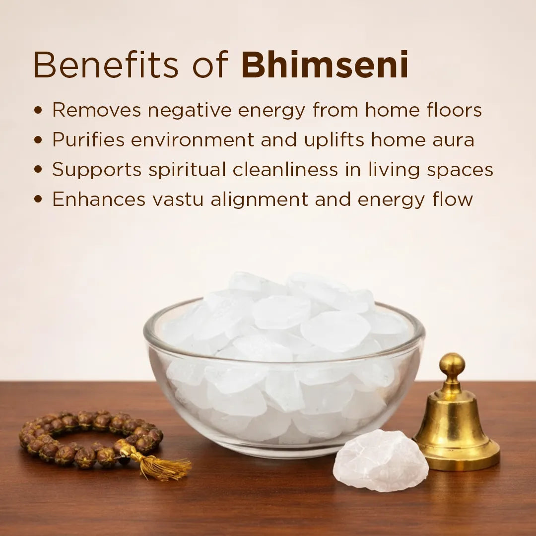 Bowl of white stones with a bell, bracelet, and crystal on a wooden surface with text about Bhimseni benefits.