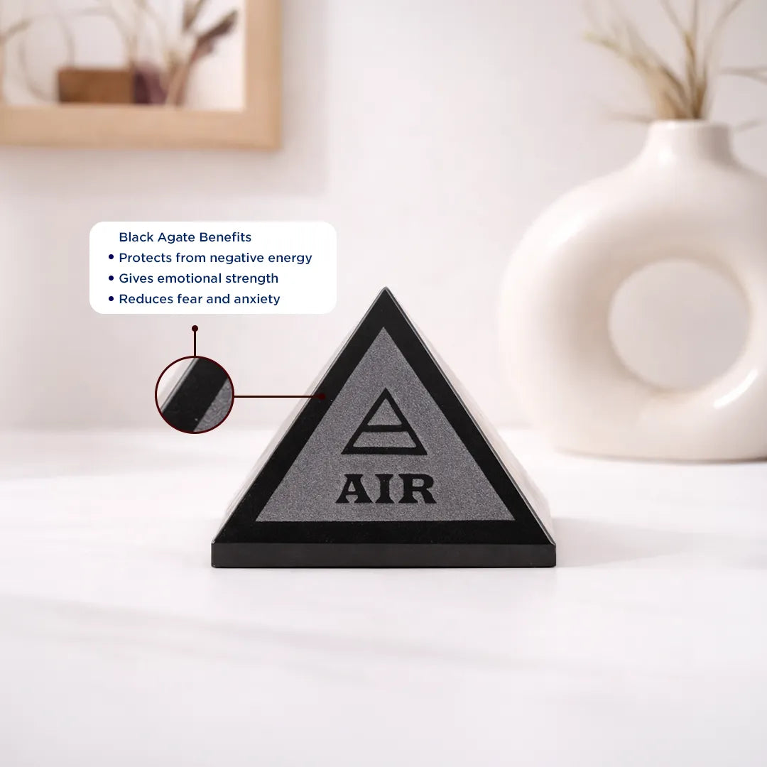 Triangular black stone with 'AIR' symbol on a white surface, surrounded by decorative items.Black Agate Five Element Pyramid – Energy Balancing Crystal Pyramid for Focus & Protection