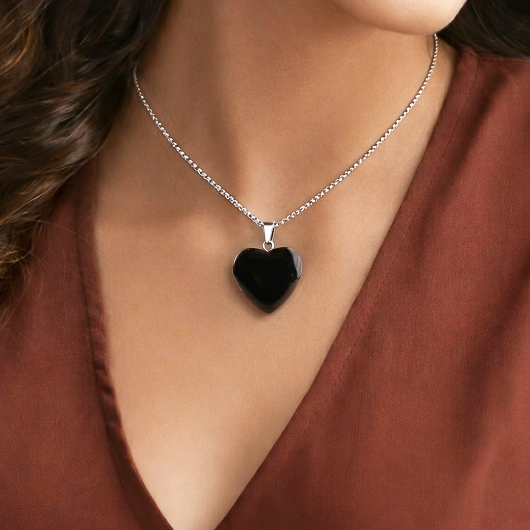 Black heart-shaped pendant on a silver chain worn by a person in a brown top.Black Obsidian Heart Pendant (Abhimantrit) for Protection & Strength