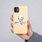 Phone case with a sticker of a face and text held by a hand against a gray background