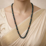 Person wearing a long beaded necklace with a neutral background