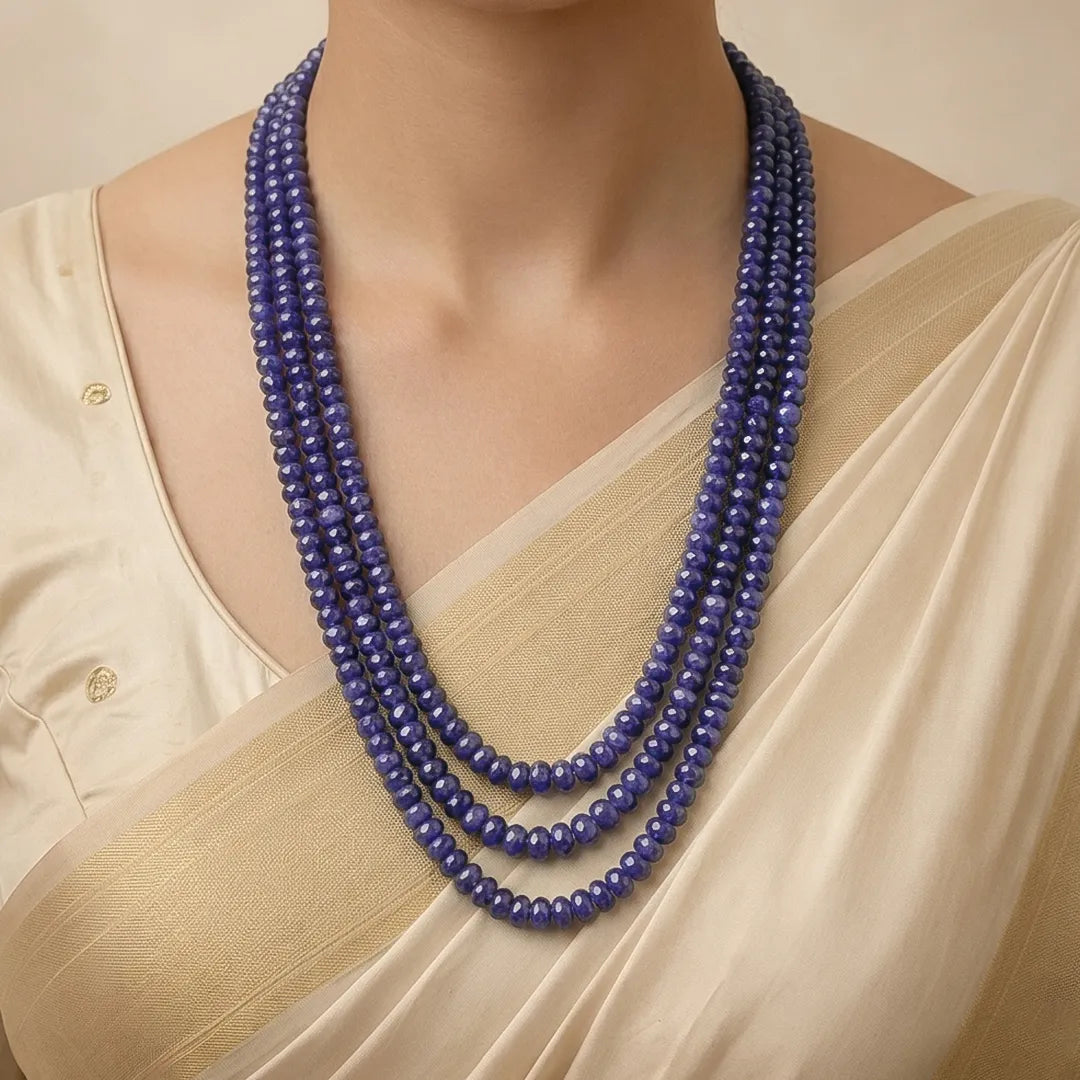 Woman wearing a beige saree with a blue beaded necklace against a neutral background