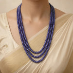 Woman wearing a beige saree with a blue beaded necklace against a neutral background