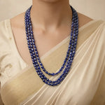 Woman wearing a long blue beaded necklace with a beige top.