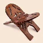 A carved wooden book stand with a rustic brown finish, featuring intricate cutout patterns and a small star detail on the front leg, set against a solid light beige background.