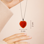 Red heart-shaped pendant necklace with measurements on a beige background
