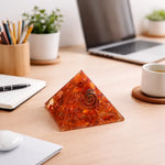 Pyramid-shaped object with a spiral design on a desk with a laptop, cup, and stationery items.