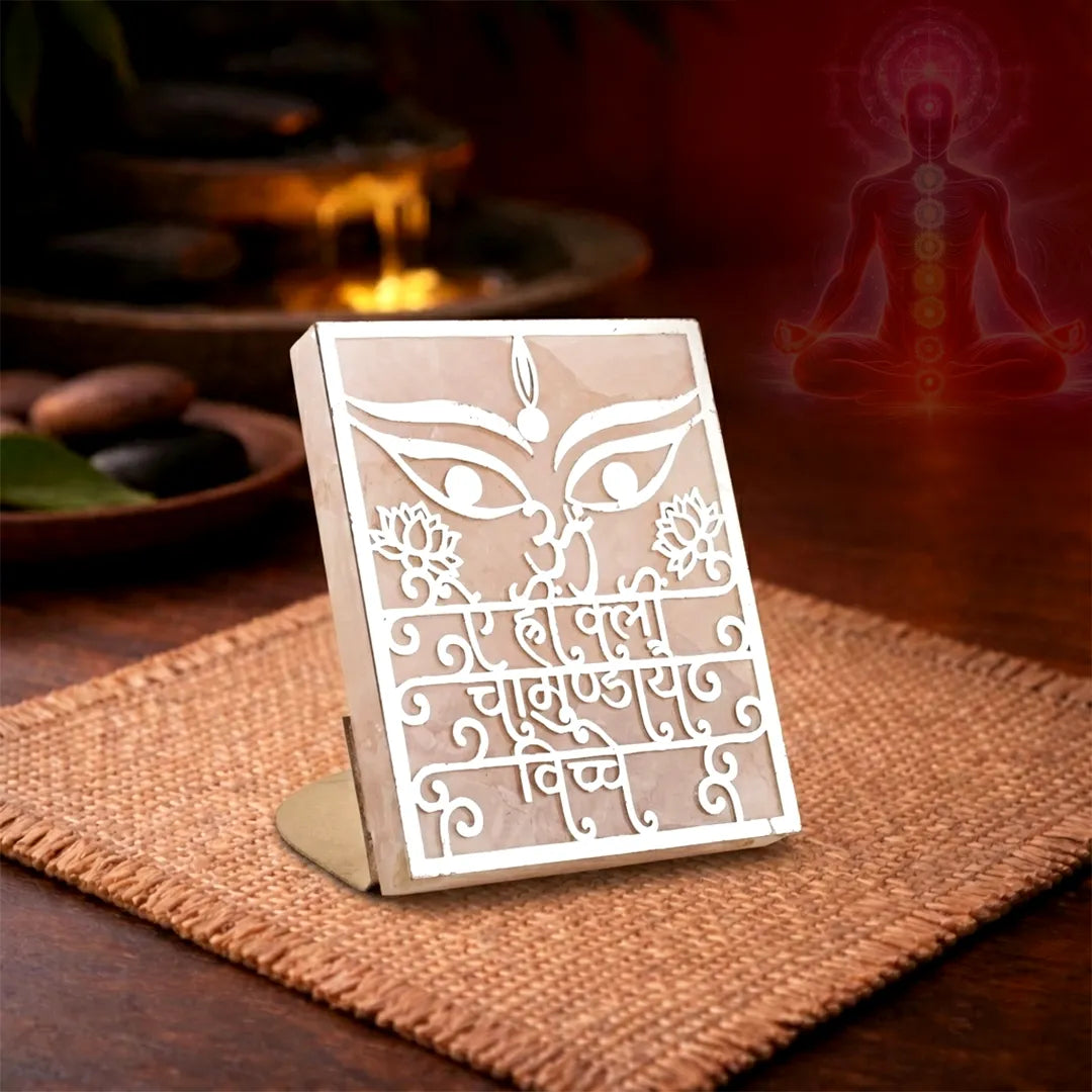 Decorative panel with intricate designs on a stand, placed on a textured surface with a blurred background.Chamunda Beej Mantra Rose Quartz Candle Stand for Protection & Healing