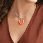 Necklace with a heart-shaped pendant worn by a person in a brown top