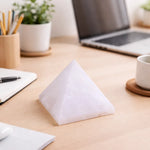 Pyramid-shaped object on a desk with a laptop, notebook, and cup in the background