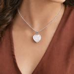 Heart-shaped silver pendant necklace on a person wearing a brown top
