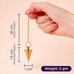 Hand holding a gold pendulum with measurements on a beige background
