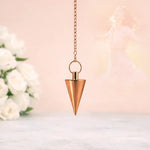 Bronze pendulum hanging against a soft, blurred background with flowers.