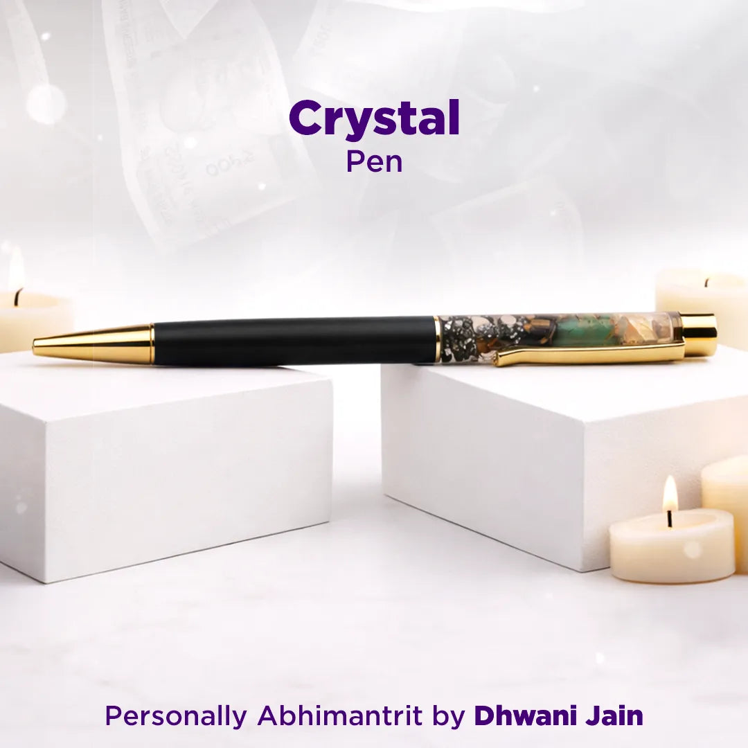 Crystal pen with gold accents on a white surface with candles, branded as 'Personally Abhimantrit by Dhwani Jain'.