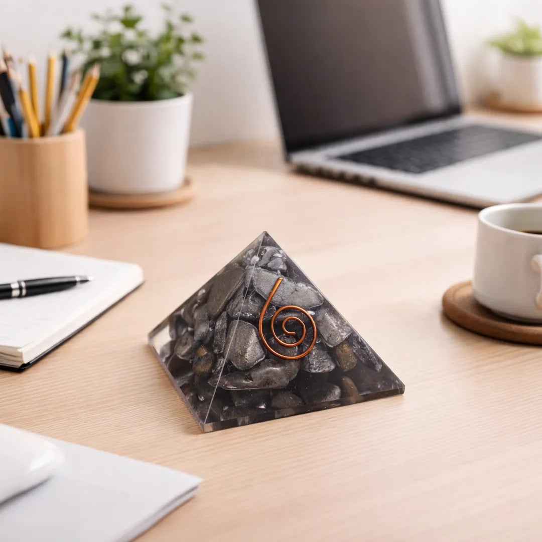 Pyramid-shaped decorative item on a desk with laptop, notebook, and cup in the background