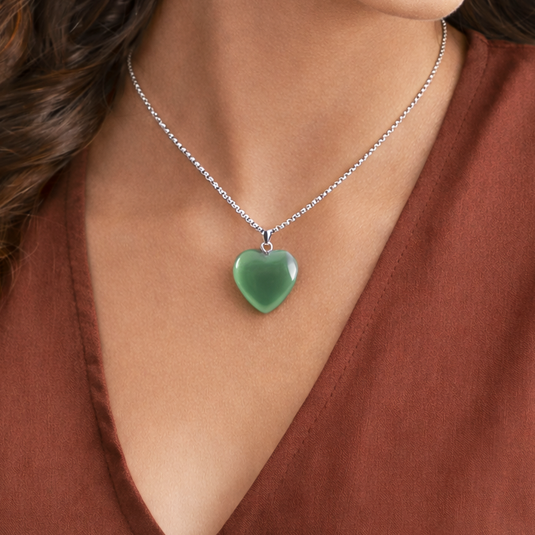 Green heart-shaped pendant on a silver chain worn by a person in a rust-colored top.