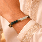 Close-up of a wrist wearing a bracelet with green and gold beads, against a neutral background.