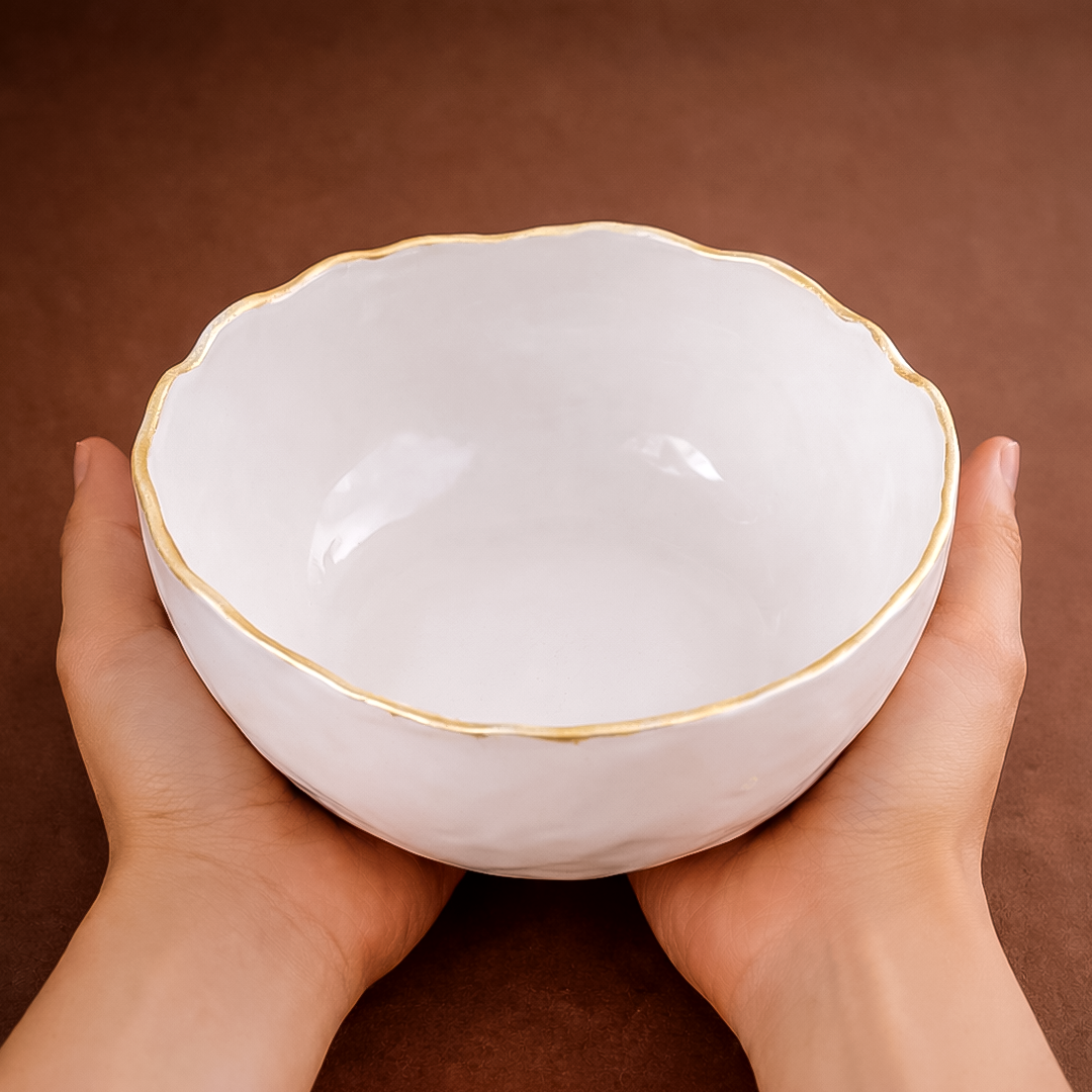 White ceramic bowl with gold rim held by hands against a brown background