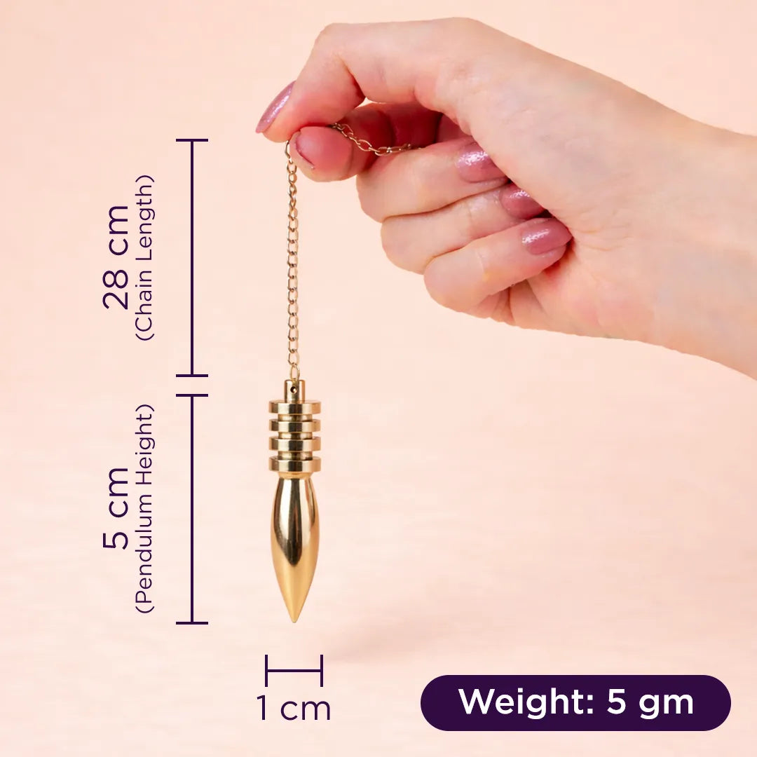 Hand holding a gold pendulum with measurements on a beige background