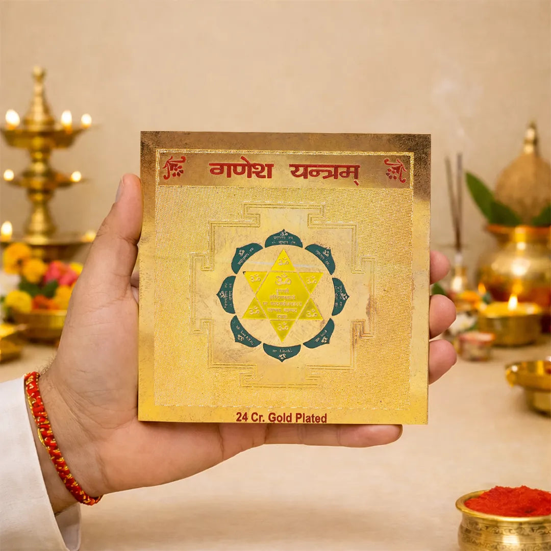 Gold-plated Ganesh Yantra held by a hand with a blurred background of religious items.Ganesh Yantra – 24K Gold Plated Vighnaharta Ganpati Yantra for Success & Protection
