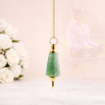 Green teardrop pendant with gold chain on a blurred floral background