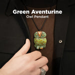 Green aventurine owl pendant on a black cord, held by a hand against a dark background.