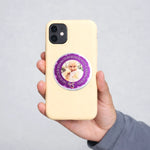 Hand holding a beige phone case with a purple circular design featuring text and an image.