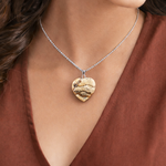 Gold heart-shaped pendant necklace on a person wearing a rust-colored top.