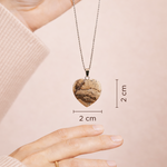 Heart-shaped pendant necklace held by a hand with measurements on a plain background