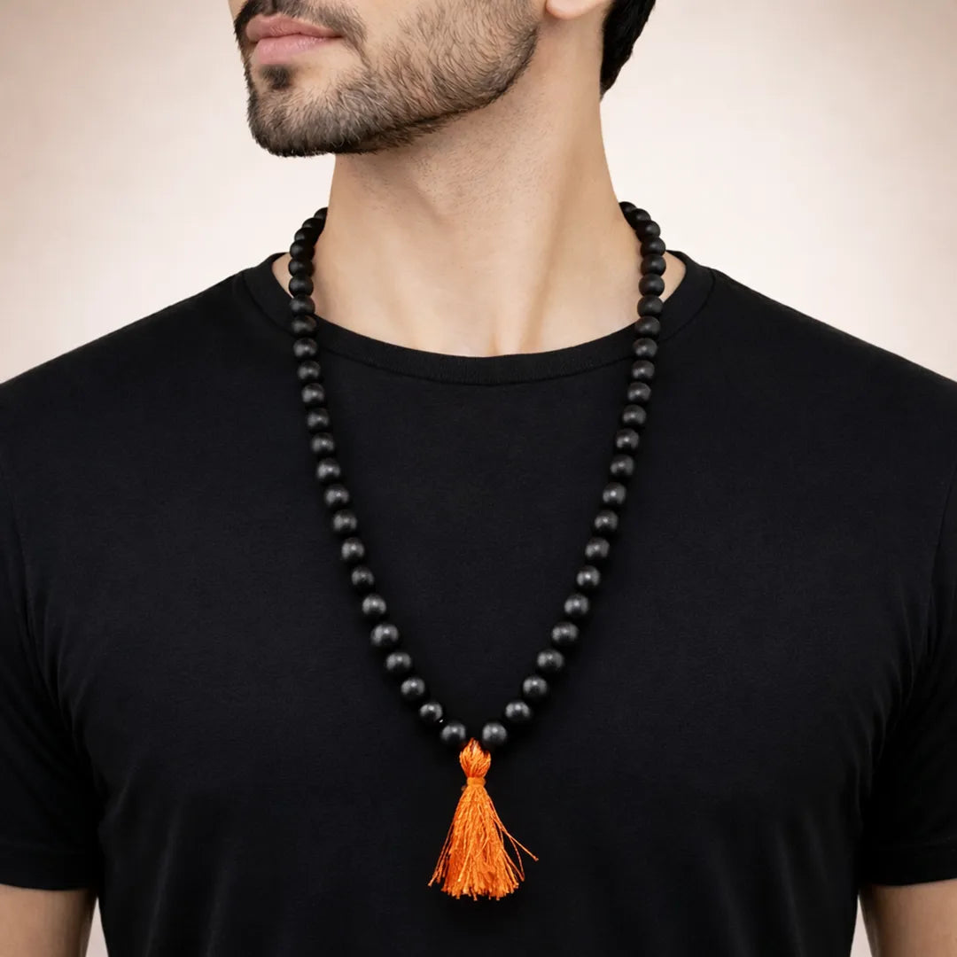 Man wearing a black beaded necklace with an orange tassel on a plain backgroundKarungali Jap Mala (Ebony Wood) for Meditation, Protection & Spiritual Focus