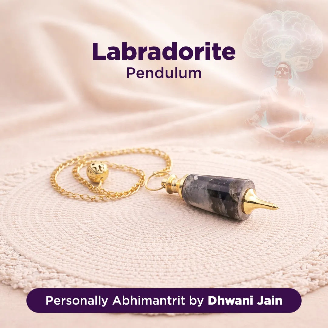 Labradorite pendulum with gold chain on a soft fabric background, branded as 'Personally Abhimantrit by Dhwani Jain'.
