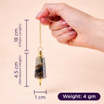 Hand holding a crystal pendulum with measurements on a beige background