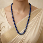 Person wearing a blue beaded necklace with a beige saree